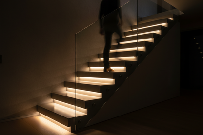 Motion sensor LED strip light glowing warm white under each stair step in dark modern home staircase at night