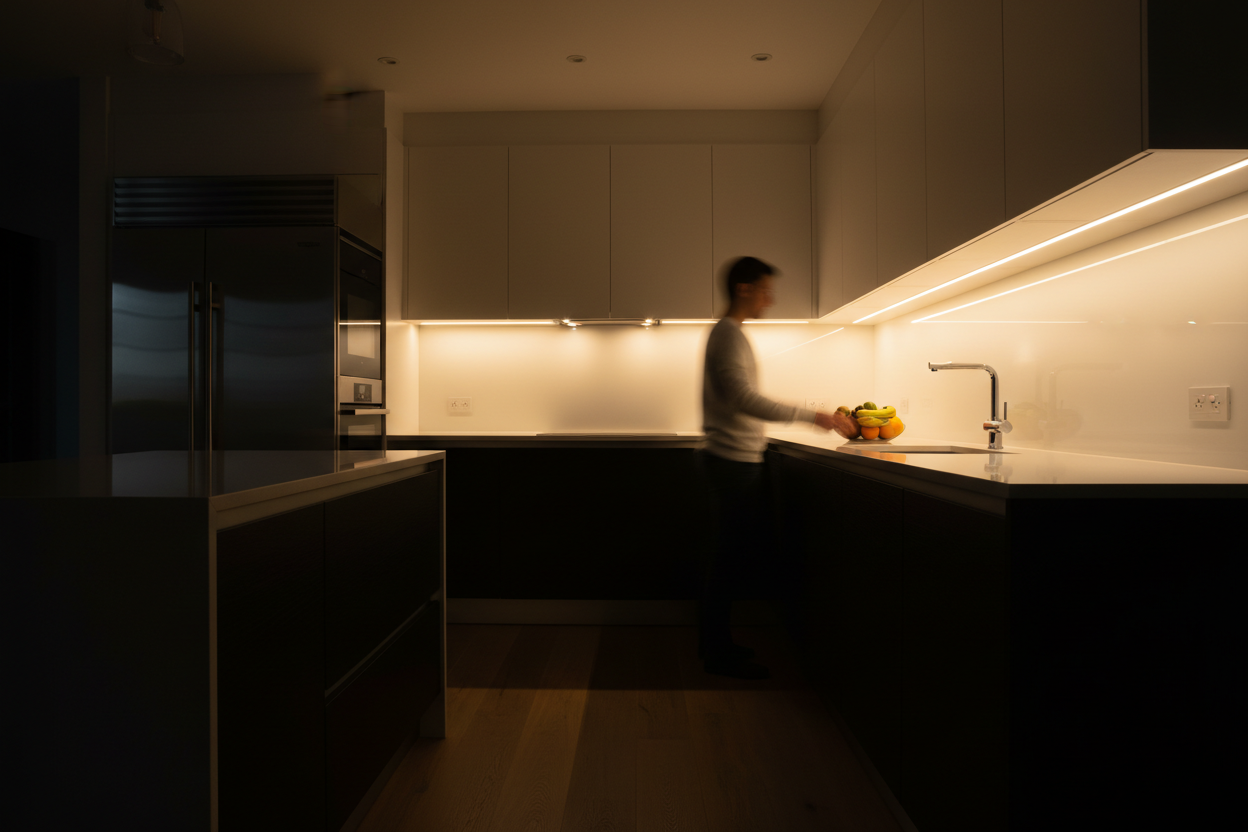 Motion sensor LED strip light glowing warm white under kitchen cabinets illuminating countertop at night